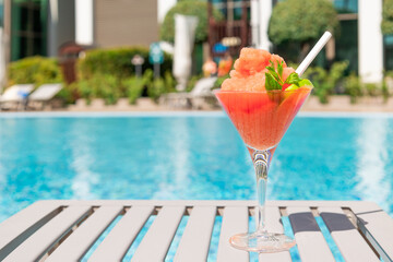 Fresh red cocktail with ice in glass on swimming pool. Tropical juice on luxury vacations. Concept summer holiday and travel.
