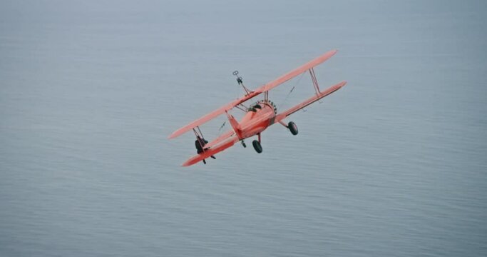 Vintage red airplane over ocean with stuntman on wings, aerial