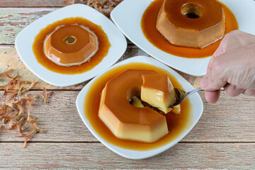 Man taking a slice with a spoon of condensed milk pudding with caramel sauce, alongside other...