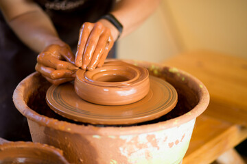 Hands of potte makes pottery dishes on potter's wheel. Sculptor in workshop makes clay product closeup