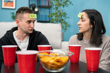 In the Living Room Diverse Couple Loving Friends Playing Who am I game With Sticky Papers Attached...
