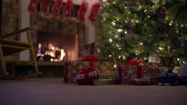Low angle, roaring fireplace behind presents under Christmas tree
