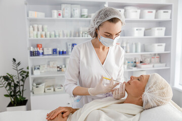 Beautician makes mesotherapy injections to a senior woman. Treatment of a woman by a beautician for...