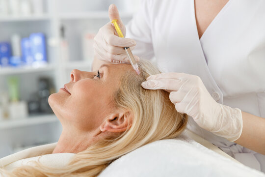 Cosmetologist does prp therapy against hair loss of a senior blond woman in a beauty salon. Cosmetology concept