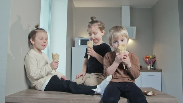 Young best friends kids eating ice-cream together in kitchen at home