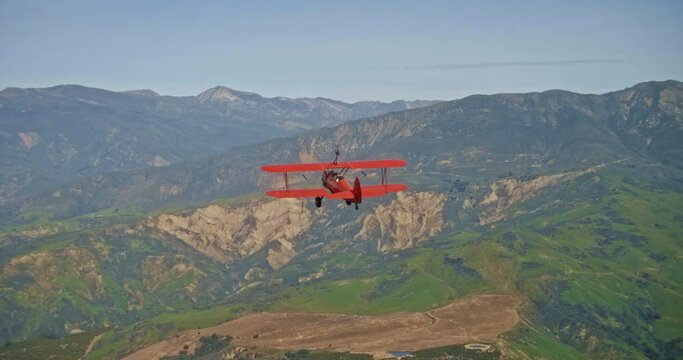 Red vintage plane flies over mountains, aerial