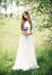 Obraz na płótnie Canvas Beautiful young woman in white wedding dress with flowers enjoying a summer day in nature