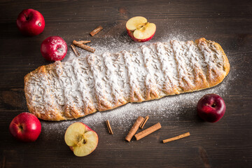 Traditional strudel sprinkled with sugar and  sunflower seeds with home grown organic red apples and whole  Ceylon cinnamon on dark wooden background