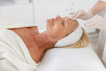 Fototapeta na wymiar Close up face spa beauty treatment, skincare. Senior woman getting facial care by beautician at spa salon, side view