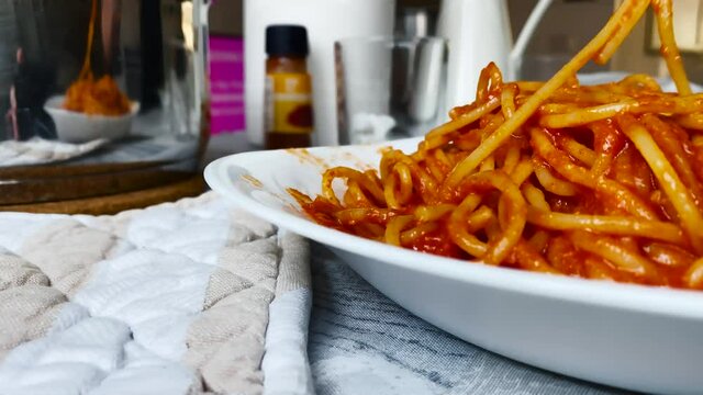 Wrapping spaghetti with tomato sauce using a steel fork.