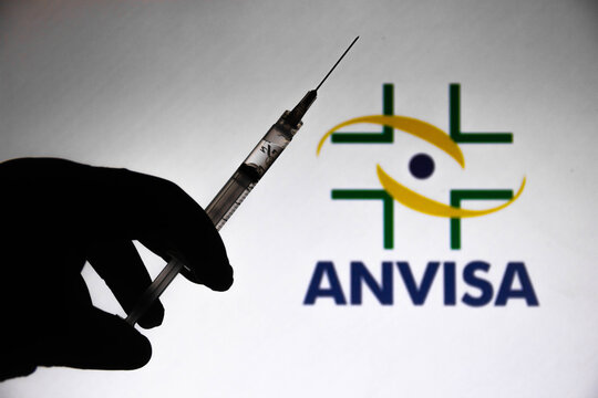 March 30, 2021, Brazil. In this photo illustration the medical syringe is seen with National Health Surveillance Agency (Anvisa) company logo displayed on a screen in the background.