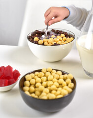 Bowl full of ready to eat healthy cereals in shape of cocoa and vanilla balls served with spoon and glass of milk