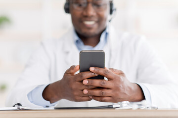 Obraz na płótnie Canvas Consultation online. African american male doctor using smartphone at workplace, messaging with his patient