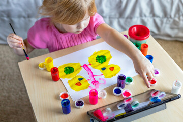 Little child painting with colorful paints sitting at the table at home