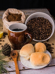 Coffe cup with coffee beans on a wooden table with bread and buns