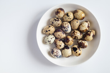 Organic quail eggs on a white plate in white table. Top view. Copy space.