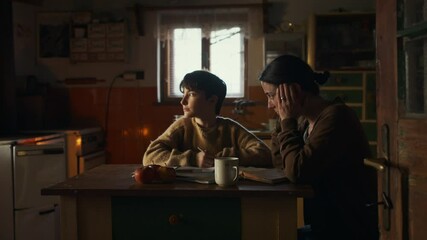 Portrait of sad poor mature mother helping small daughter with school indoors at home, poverty concept.