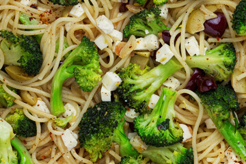 Close-up top view of spaghetti pasta with broccoli vegetable, olives and cheese.