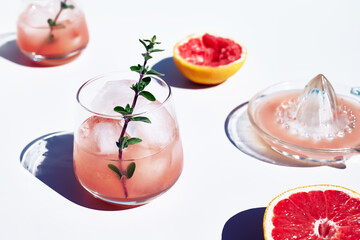 Summer grapefruit cocktail. Fresh healthy grapefruit beverage with herbs on sunlight with hard shadows. Creative drink on white background.