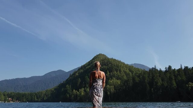 Woman walk on water on pier in sunglasses and a boho silk shawl. Girl rest on flood wood underwater dock. The pavement is covered with water in lake.