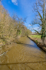 Fototapeta na wymiar Geul river with its brown waters among bare trees and wild plants, sunny day with a blue sky in Valkenburg aan de Geul municipality in South Limburg, the netherlands