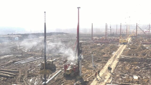 Excavation at a construction site, diesel pile driving machine with rumble and smoke drives piles deep into the ground to ensure the strength of the foundation of the future structure