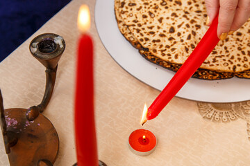 A woman's hand holds a candle for the Passover Seder and lights it from a burning fire.