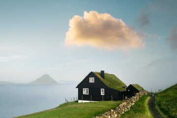 Foggy morning view of a house with typical turf-top grass roof and beauty sunset cloud in the Velbastadur village on Streymoy island, Faroe islands, Denmark. Landscape panorama