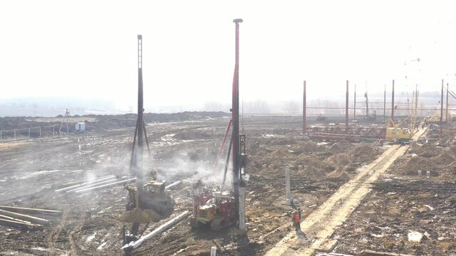 Excavation at a construction site, diesel pile driving machine with rumble and smoke drives piles deep into the ground to ensure the strength of the foundation of the future structure