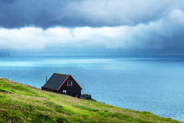 Black house on famous faroese Witches Finger Trail and Koltur island on background. Sandavagur village, Vagar island, Faroe islands, Denmark. Landscape photography