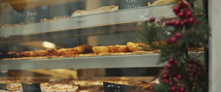 Cafe shop window display in Lisbon, Portugal during a winter holiday season. Traditional Portuguese egg tart pastry. Slow motion.