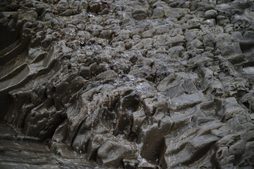 Mini waterfall close up in mountains. Thin stream of water flows down gray textured rock. Natural natural spring with clean drinking water.