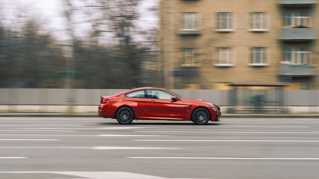 Red aggressive BMW Sport Car riding on the road. Side view of shiny bmw M4 F82 driving in the street.