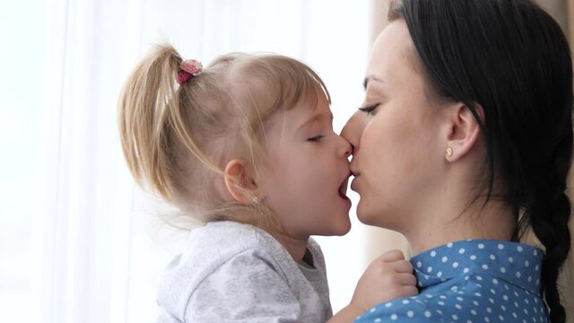 A little girl kisses her beloved mother, mom holds the child in her arms and hugs, the concept of a happy family life, the nanny calms the child, the parent is next to the kid together, 4K, close-up