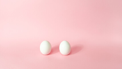 Two white chicken eggs isolated on light pink pastel background. Happy Easter Day.