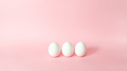 Three white chicken eggs isolated on light pink pastel background. Happy Easter Day.