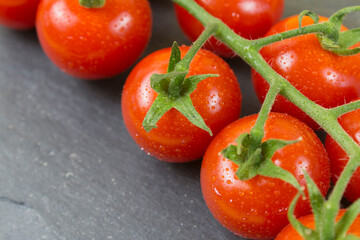 branch of small red tomatoes on black stone background. Close up.