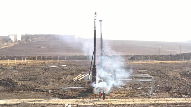 Excavation at a construction site, diesel pile driving machine with rumble and smoke drives piles deep into the ground to ensure the strength of the foundation of the future structure