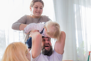 Dad and daughter play with the baby, holding him on his head.