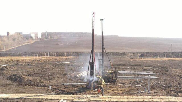 Excavation at a construction site, diesel pile driving machine with rumble and smoke drives piles deep into the ground to ensure the strength of the foundation of the future structure