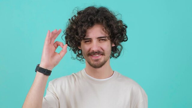 Close up of a positive curly haired young man showing ok gesture with fingers.