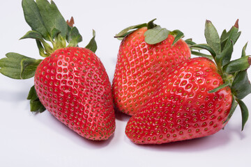 Photo of three fresh red strawberries with strawberry leaf isolated on white background