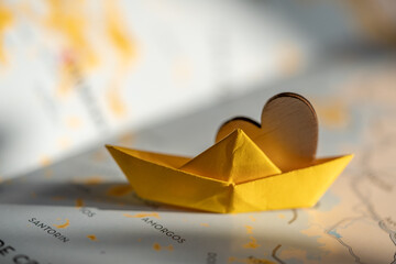 isolated origami yellow boat with wooden heart on world map. travel, sail or cruise concept, shipping or transportation through the sea. 