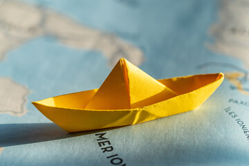 isolated origami yellow boat on world map. travel, sail or cruise concept, shipping or transportation through the sea. view from above