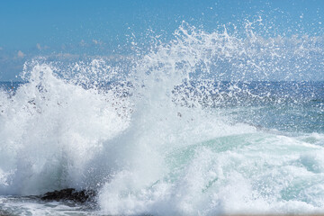 Waves crashing over black rocks in frozen motion on a warm sunny summer day. Blue and white sea colors. Rainbow Bay, Gold Coast, Queensland, Australia.