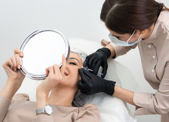 Cosmetologist making injection in eye. Young woman gets beauty facial injections. Face rejuvenation...