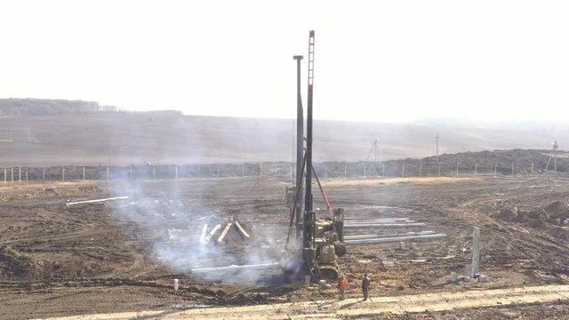Excavation at a construction site, diesel pile driving machine with rumble and smoke drives piles deep into the ground to ensure the strength of the foundation of the future structure
