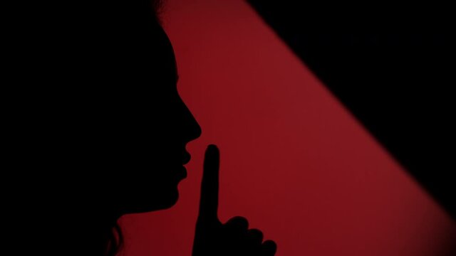 Side view of faded female face placing her finger on lips on dark red background