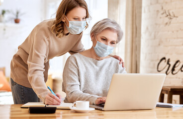 Anonymous women in masks using laptop and taking notes at home