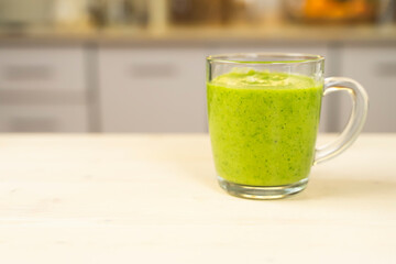 Glass cup with green spinach and kale health smoothies with straw in kitchen table